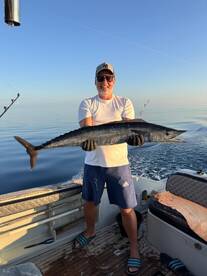 Angler proudly displaying a large Wahoo caught during a serene morning fishing trip on a boat.