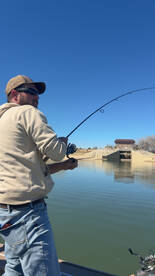 An angler actively reeling in a catch from a boat on a calm lake, showcasing the excitement of fishing in a serene environment.