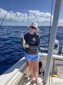 A smiling angler proudly displays a small Yellowtail Snapper while fishing on a sunny day in open waters.