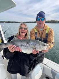 Happy anglers displaying a large Striped Bass while enjoying a day on the water.