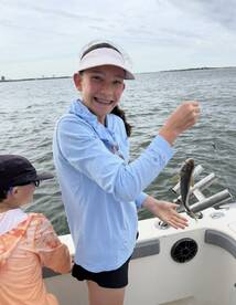 A young angler joyfully displaying her catch, a small fish, while fishing on a boat, showcasing a fun family outing.