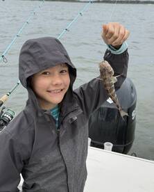 A young angler proudly displaying a small fish while fishing on a boat, showcasing a fun day on the water.