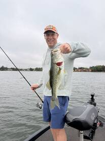 Angler proudly displaying a large Largemouth Bass while fishing on a calm lake.