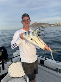 An angler proudly displaying a beautiful Roosterfish while fishing off the coast, showcasing the stunning ocean backdrop.