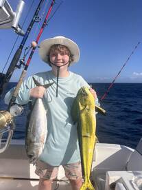 A young angler proudly displaying a large Mahi Mahi and a Tuna while fishing offshore, showcasing a successful day on the water.