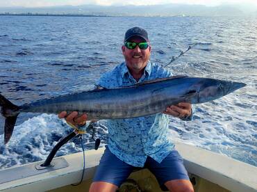 Angler proudly displaying a large Wahoo while fishing offshore, showcasing a successful day on the water.