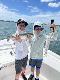 Two young anglers proudly displaying their catches of speckled trout while enjoying a day of fishing on a boat.