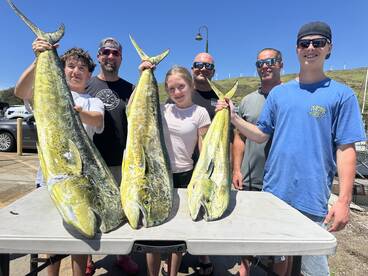 A family group proudly displaying their catch of large Mahi Mahi after a successful fishing trip.
