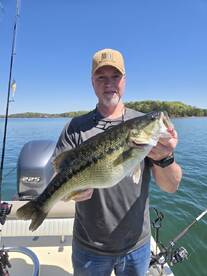 An angler proudly displaying a large Largemouth Bass while fishing on a serene lake.