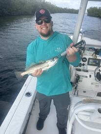 Angler proudly displaying a Speckled Trout while fishing from a boat in a scenic waterway.