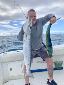 Angler proudly displaying a Barracuda and a Mahi Mahi while fishing on a boat in open waters.