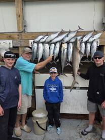 A group of anglers proudly displaying their catch of various fish, including a shark, on a catch board after a successful fishing trip.