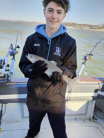 A young angler proudly displaying a caught Speckled Trout while fishing on a boat.