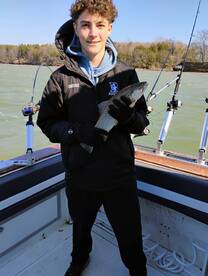 Young angler proudly holding a trout while fishing on a boat, showcasing a successful catch on a scenic day.