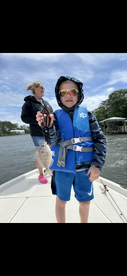 A young angler proudly displaying a caught fish while fishing with family on a boat in a scenic waterway.