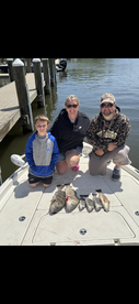 A family proudly displaying their catch of several fish, including Redfish, on the bow of a boat after a successful fishing trip.