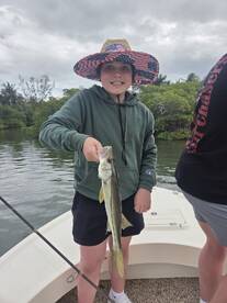 A young angler proudly holding a Snook while fishing in a scenic coastal environment.