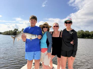 A young angler proudly holding a large Tarpon while posing with family on a boat in a scenic waterway.