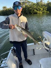 Young angler proudly holding a Snook while fishing from a boat in a scenic coastal environment.
