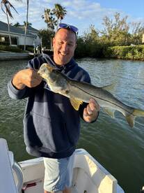 Angler proudly displaying a Snook caught while fishing from a boat in a scenic waterway.