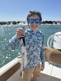 Young angler proudly holding a fish while aboard a boat, enjoying a sunny day on the water.