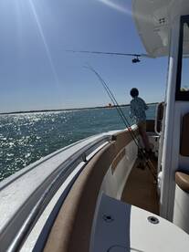 A young angler casting a line from a modern boat under a bright blue sky, enjoying a day of fishing on the water.