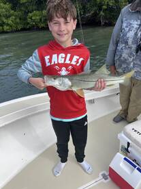 A young angler proudly displaying a Snook caught while fishing in a scenic mangrove area.