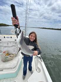 A young angler joyfully holding a small shark on a fishing boat, showcasing a successful catch during a day on the water.