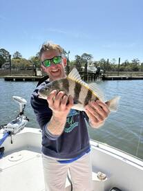 Angler proudly displaying a Black Drum caught while fishing from a boat in a scenic waterway.