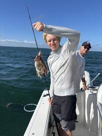 A young angler proudly displaying a caught fish while fishing on a boat, enjoying a sunny day on the water.
