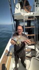 Angler proudly displaying a freshly caught fish aboard a fishing boat, enjoying a sunny day on the water.