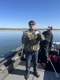 A young angler proudly displaying a caught fish while fishing on a boat, with a clear blue sky and calm waters in the background.