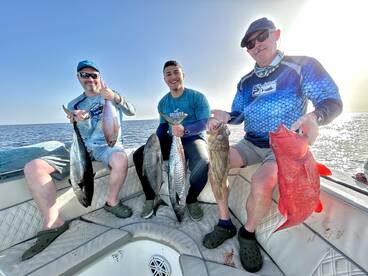 Three anglers proudly displaying their catch, including a vibrant red grouper and other species, while enjoying a day on the water.