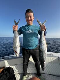 Angler proudly displaying two large fish, a King Mackerel and a Grouper, while fishing offshore.