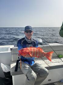 Angler proudly displaying a vibrant Red Grouper while seated on a boat in open waters.