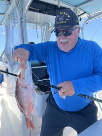 An angler proudly displaying a freshly caught Red Snapper aboard a fishing boat, showcasing a successful day on the water.