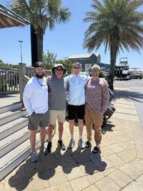 Group of four friends posing together outside a boating center, enjoying a sunny day.