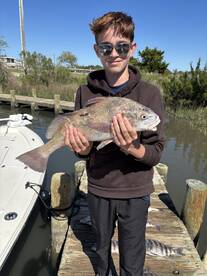 Young angler proudly holding a large fish on the dock, showcasing a successful day of fishing.