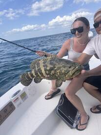 Anglers proudly displaying a large Grouper while fishing in open waters.