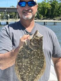Angler proudly displaying a large Flounder caught during a sunny day at the dock.