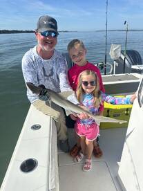 A proud family moment on the water, showcasing a caught shark with two children and an adult on a fishing trip.