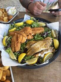 A plate of assorted fried fish and sides, showcasing a variety of seafood dishes, likely enjoyed after a fishing trip.