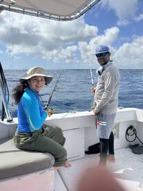 A young angler and an adult fishing together on a boat, enjoying a day of deep-sea fishing in clear blue waters.