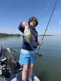 A young angler proudly displaying a Crappie while fishing on a calm lake, showcasing a beautiful day on the water.