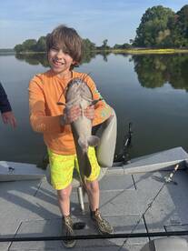 A young angler proudly displaying a catfish while fishing on a calm river, showcasing a fun family outing.