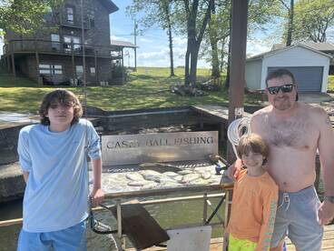 A family enjoying their fishing trip, posing with a catch of crappie displayed on a board at the dock.