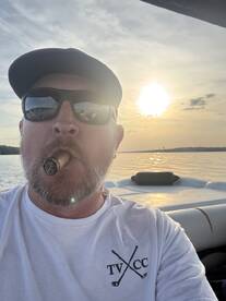A man enjoying a sunset on a boat, holding a cigar, with a scenic view of the water.