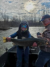 A smiling angler proudly displays a large trout while fishing on a river, showcasing a fun day out with friends.