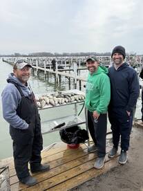 Three anglers proudly posing with their catch of fish displayed on a board at the dock, showcasing a successful fishing trip.