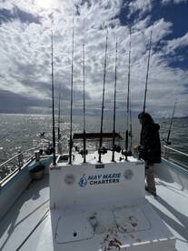 The interior of the May Marie Charters boat features multiple fishing rods set up for an exciting day on the water, with a scenic backdrop of the ocean and cloudy sky.